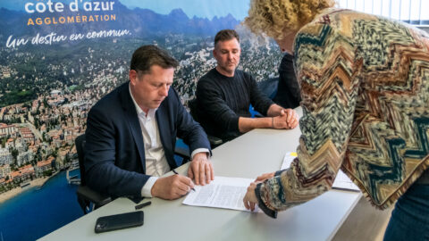 Frédéric Masquelier assis à une table signant un document, avec 2 personnes l'entourant